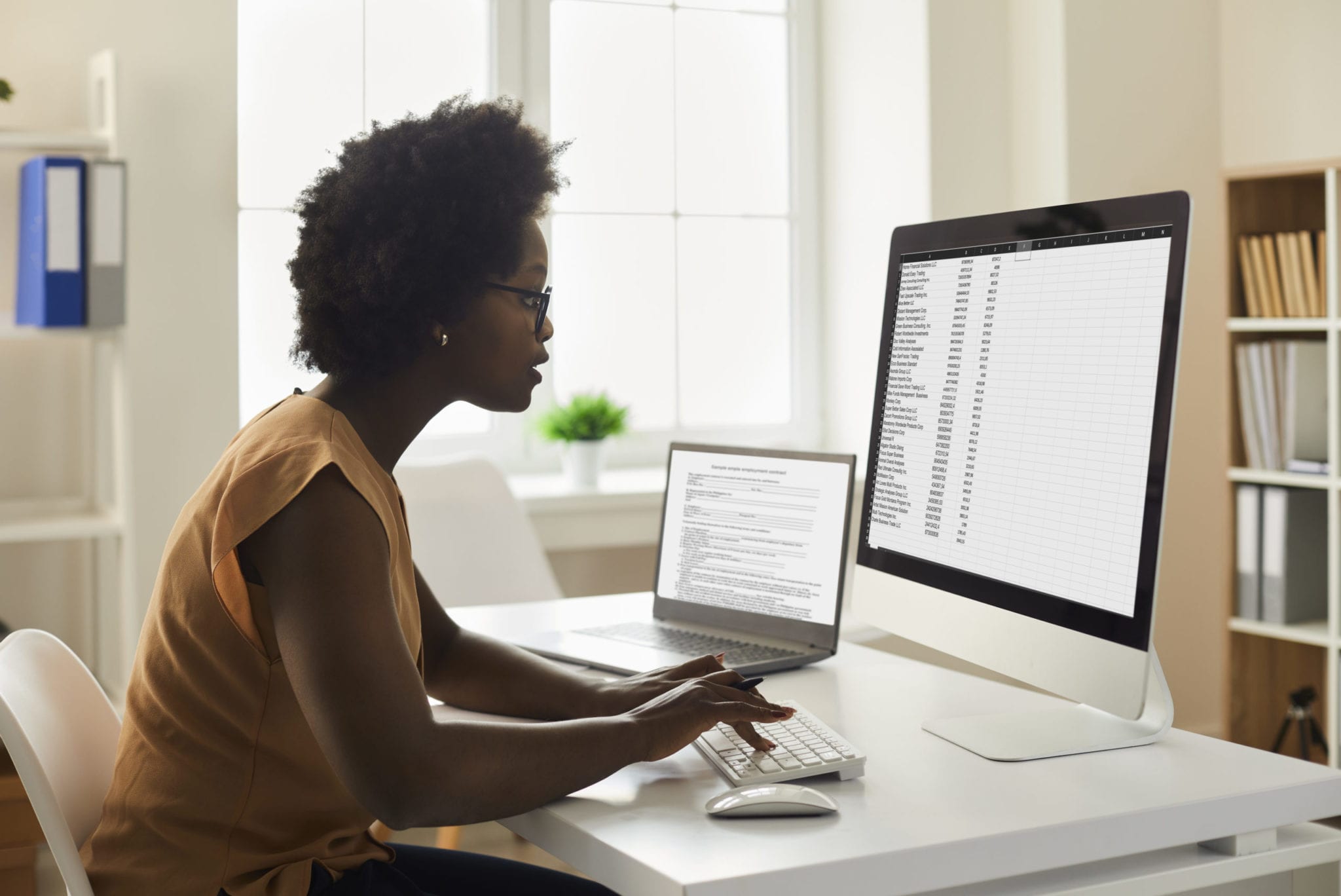 Young African-American woman sitting at office desk and working with data on computer